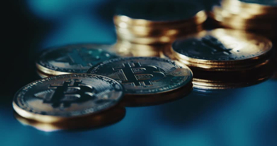 Close up of the shiny engraved surface of golden bitcoin physical coins over a reflecting surface
