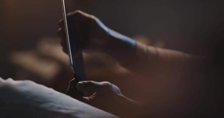 Man with brown turtleneck sweater and jeans lies on couch playing game on tablet