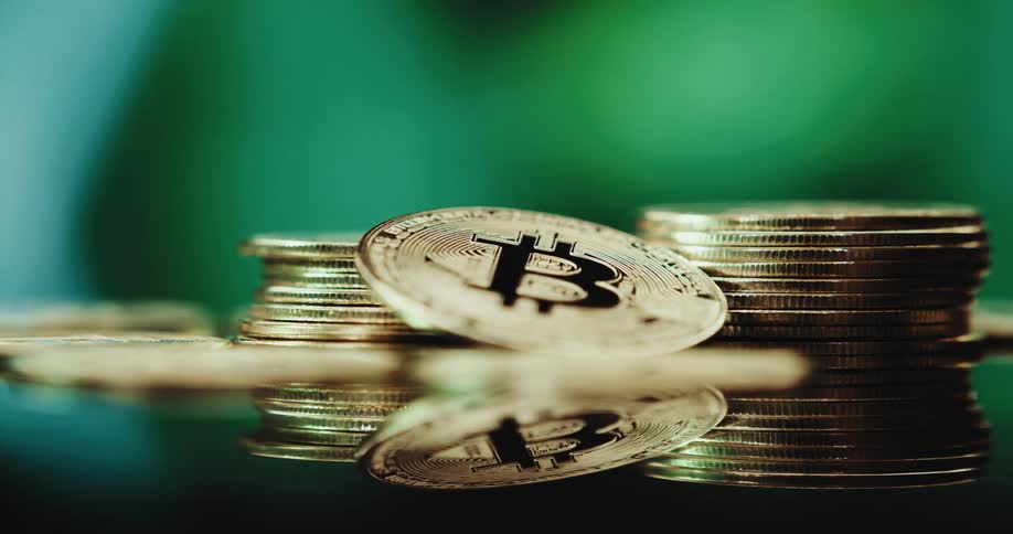 Close up of the shiny engraved surface of golden bitcoin physical coins over a reflecting surface