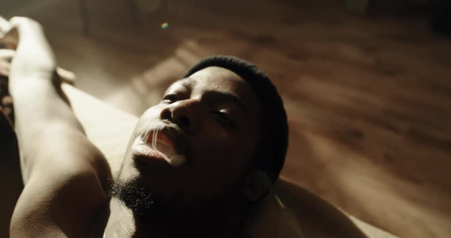 Young man laying in the couch at home smokes a cigarette watching the smoke rise at morning