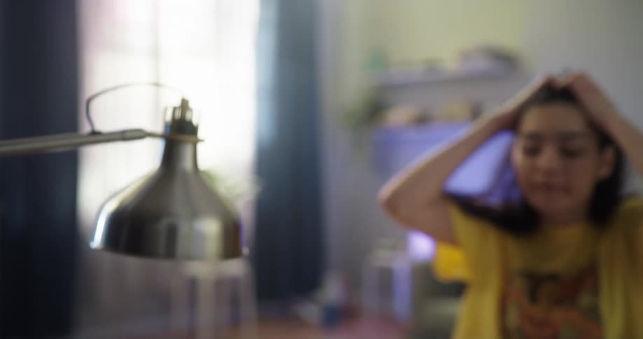 A young woman carries a coffee cup to a desk and opens her laptop at home during the day