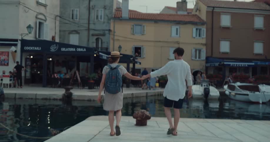 A man and woman traveling laugh as they walk on a pier and hold hands and hug and kiss