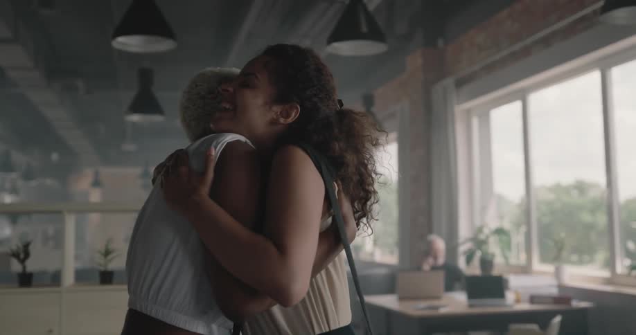 Woman sitting and talking stands to greet new woman with a hug