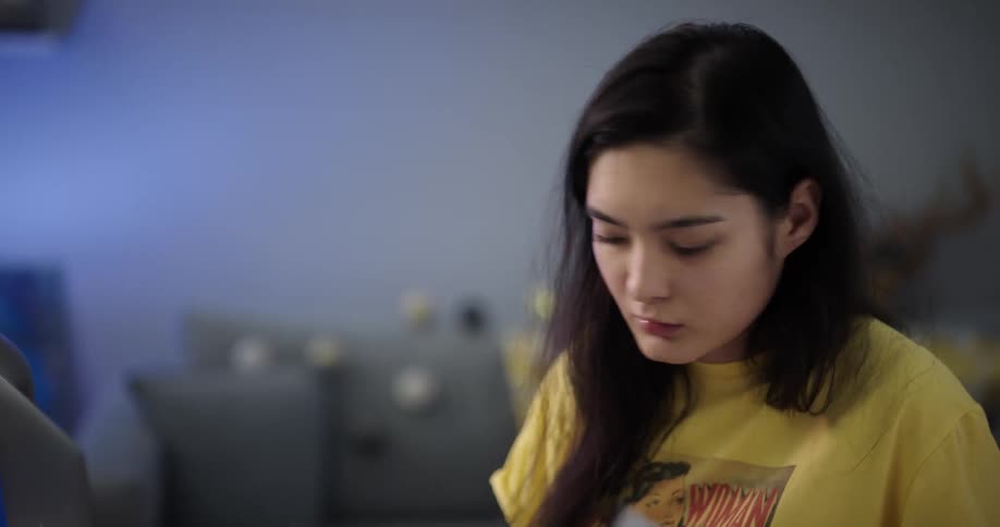 A young woman opens up her laptop to start studying in her bedroom