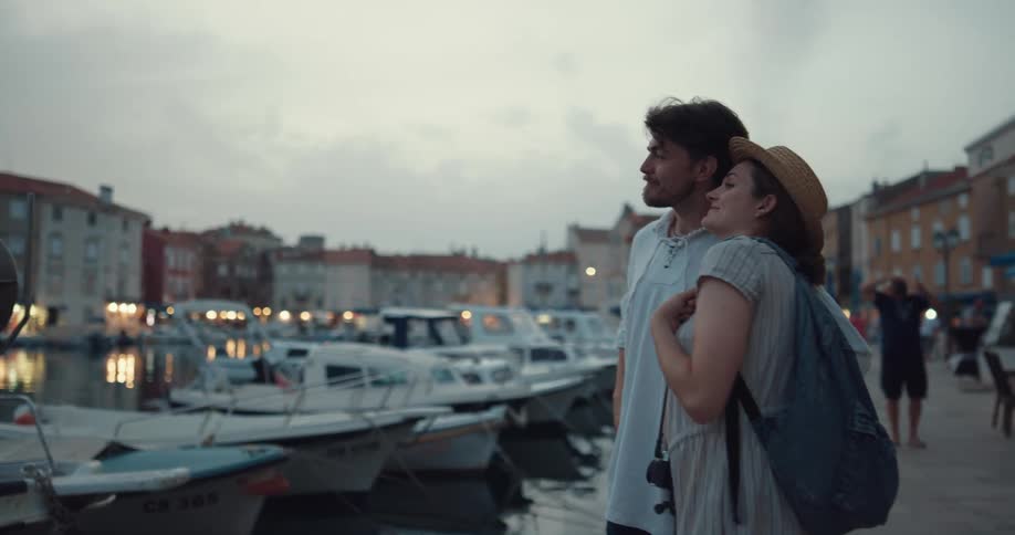 A woman uses a camera to take a photograph of a marina before being kissed by her partner