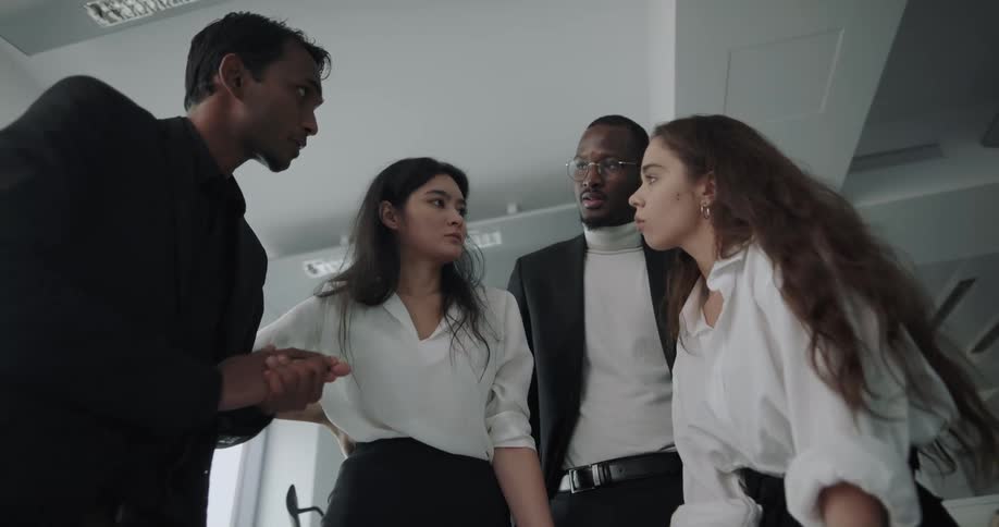 Two men and two women talk as they look down at something in the office