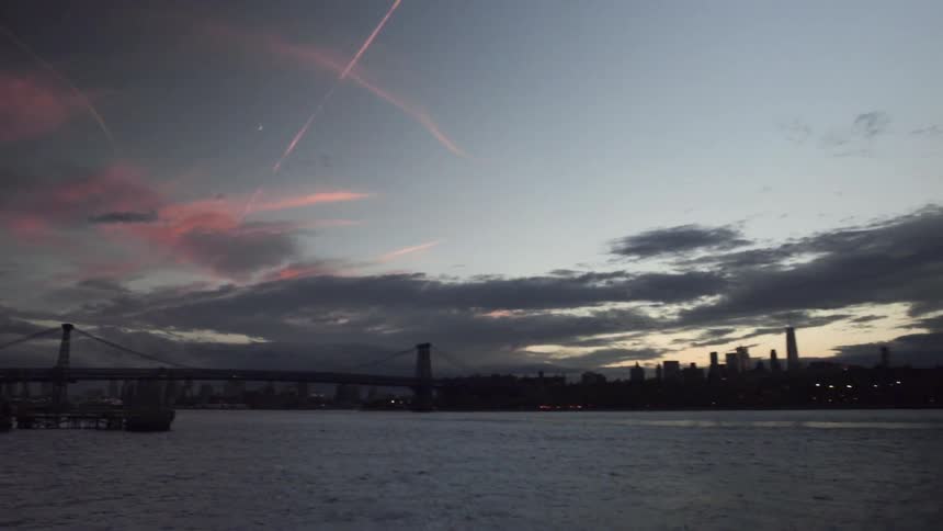 Contrails and clouds over a city skyline, bridge and harbor