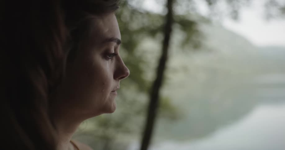 Woman standing outdoors near a lake and crying