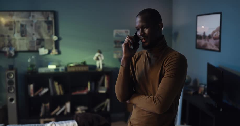 A man talks on a smartphone while standing in a house