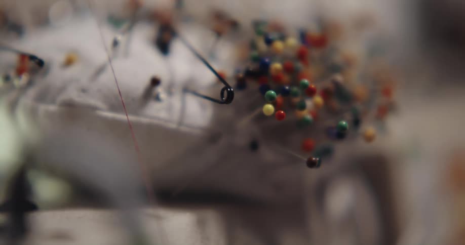 A person pulls a pin from a pin cushion covered in colorful pins