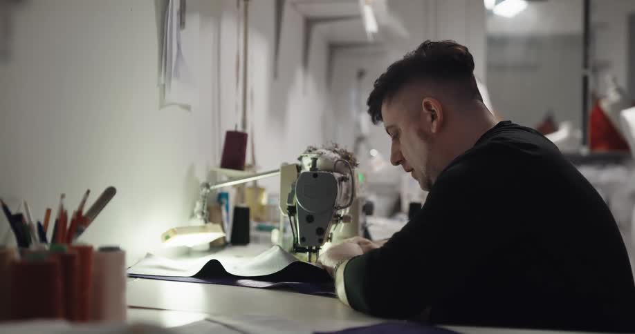 Tailor with black sweatshirt uses sewing machine in tailor shop