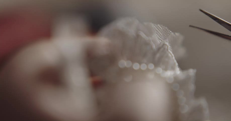 A designer carefully cuts the lace trim of their project using a small pair of scissors