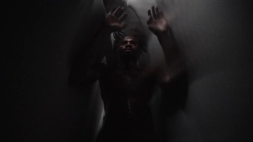 Young strong muscular shirtless man raises his hands to push back against people attacking him through fabric walls