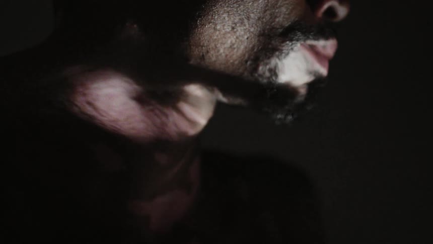 Distorted frantic eerie footage of a shirtless man standing inside a dark room