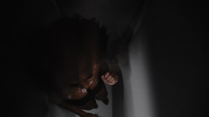 Warped footage of a nervous woman surrounded by moving walls in a dimly lit room