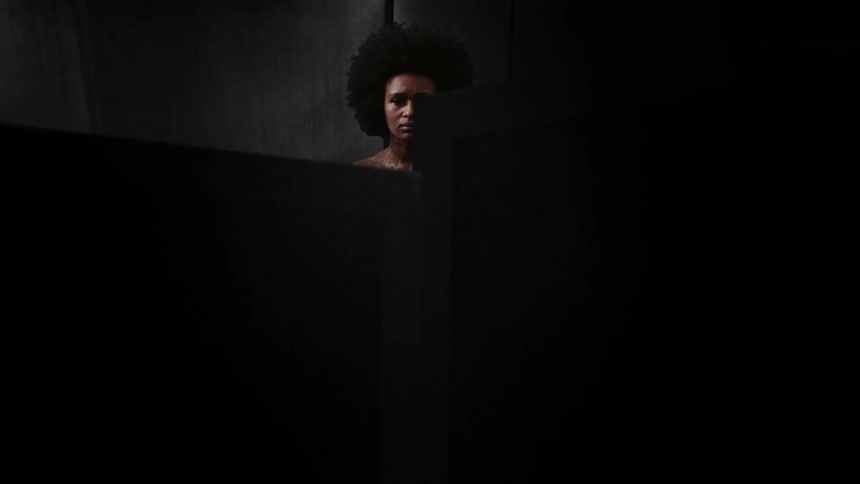 A woman stands alone in minimal clothing while a dark box encloses her