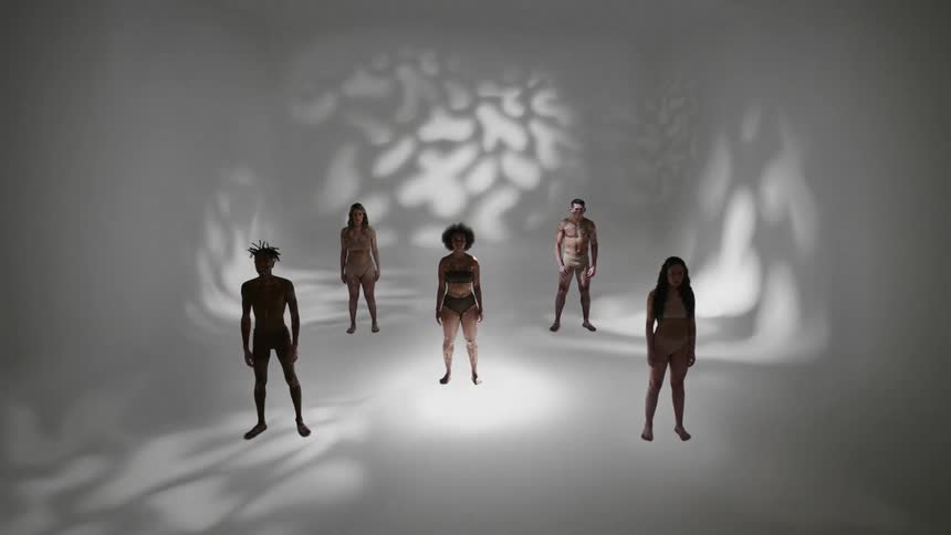 People wearing underwear stand in a curved room as patterned shadows are cast onto the walls