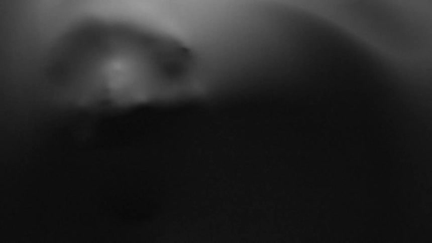 An eerie scene shows a face pushing against an elastic membrane in a darkened space
