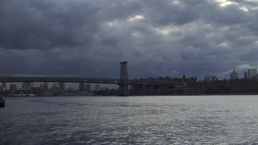 Dark storm clouds hovering above a city skyline, bridge and harbor
