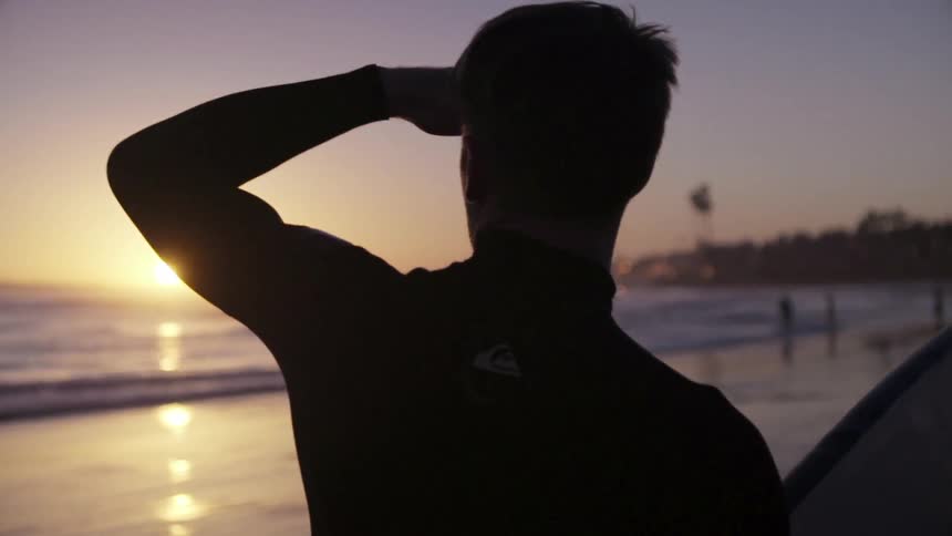 A man is walking on the beach at sunset