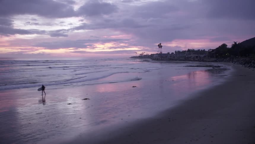 A man carrying a surfboard is walking on the beach