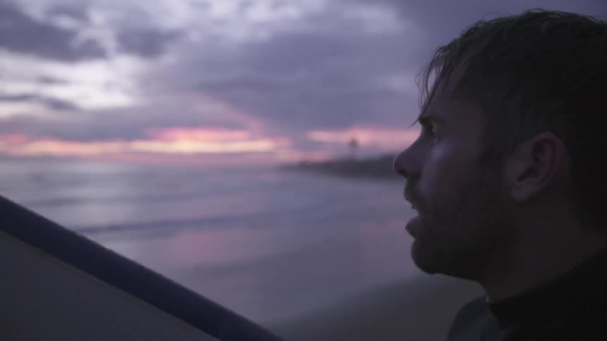 A man looks across the ocean at sunset