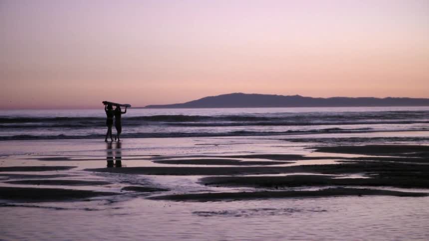 Two people carry a board across the beach
