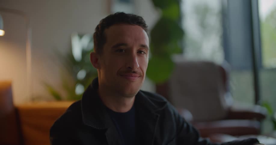 Man with mustache naval blue jacket and shirt smiles at camera in living room at home