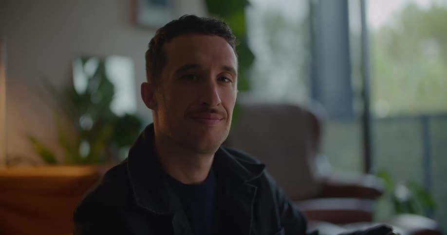 A man smiles into the camera while sitting indoors during the day