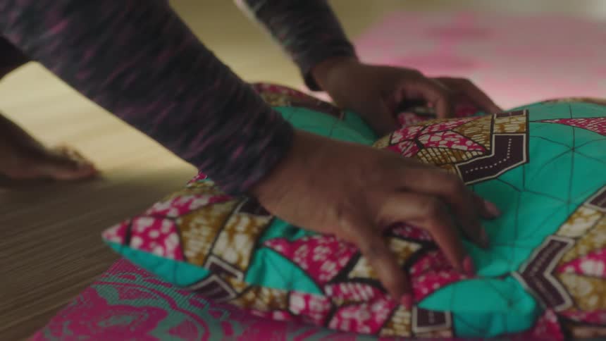 Woman rotates small colorful pillow sitting on the floor and smooths it