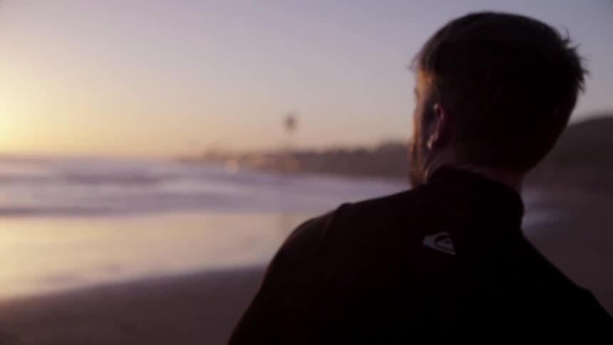 A man is walking along the beach carrying a surfboard