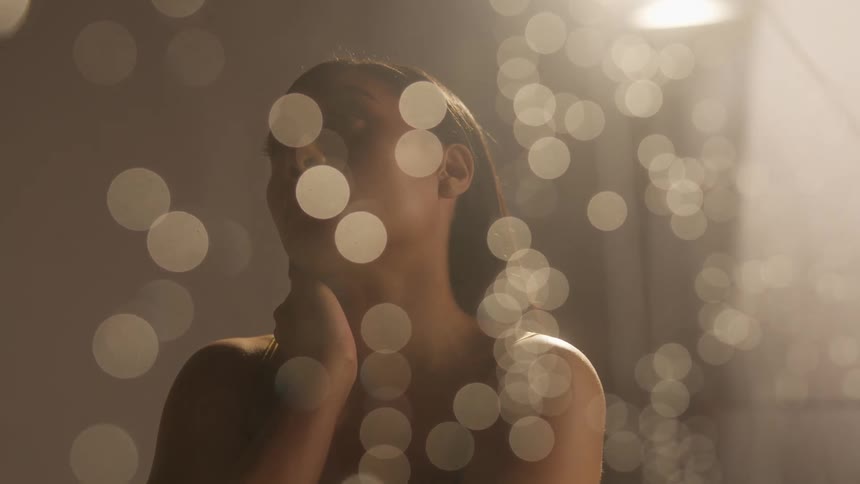 Woman stands looking out as raindrops fall down window glass