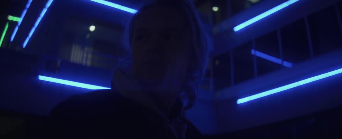 Silhouette of a woman standing in front of the blue neon lights on a building at night
