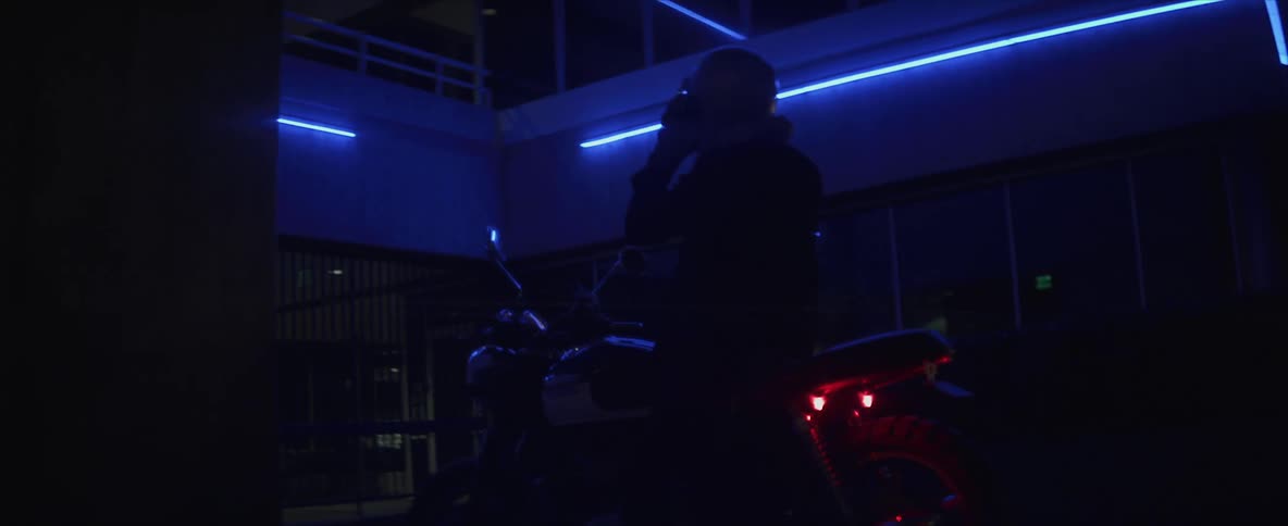 A motorcyclist pulls up to a building at night and removes their helmet