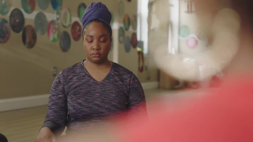 Woman shrugs her shoulders as she sits meditating across from another woman
