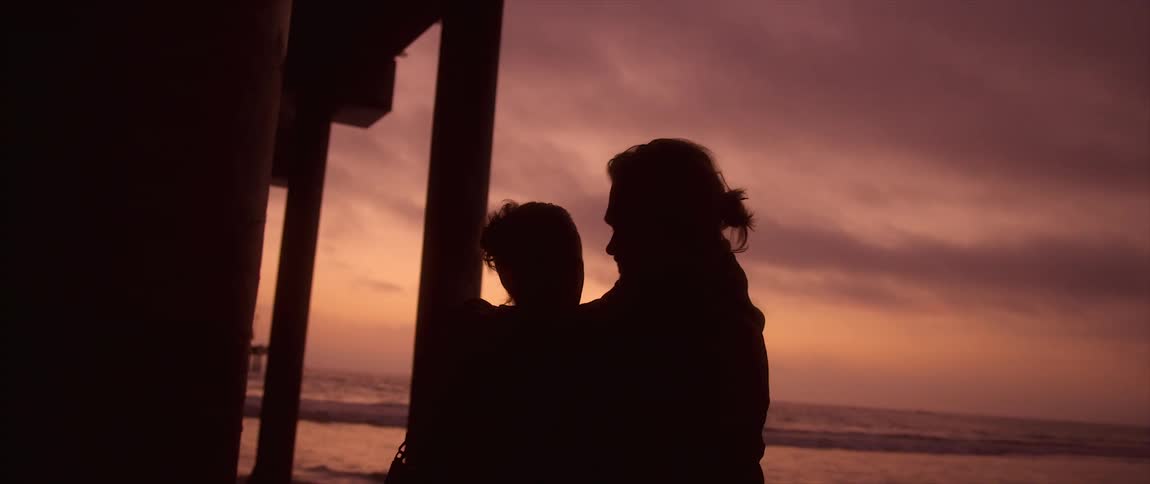 Silhouette of a young couple hugging under a pier on the beach next to the ocean at sunset