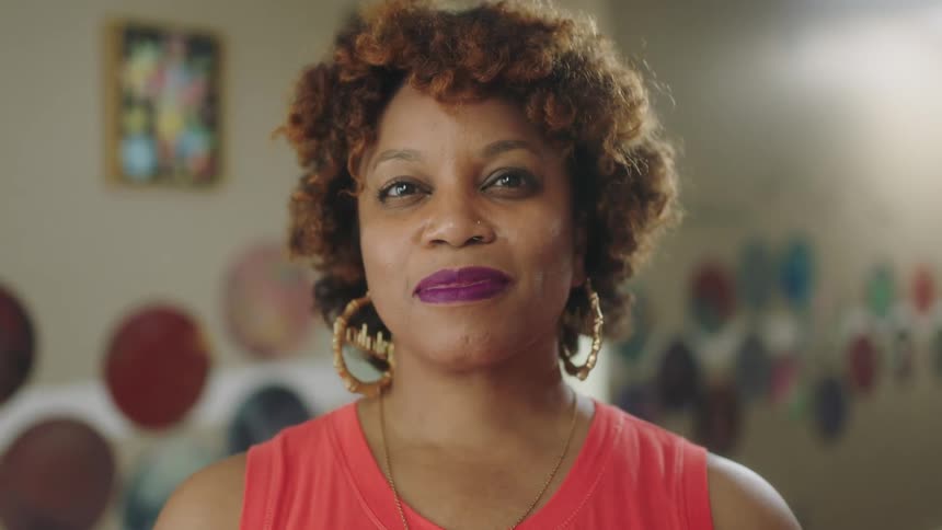 A black woman with purple lipstick smiles as she poses for the camera