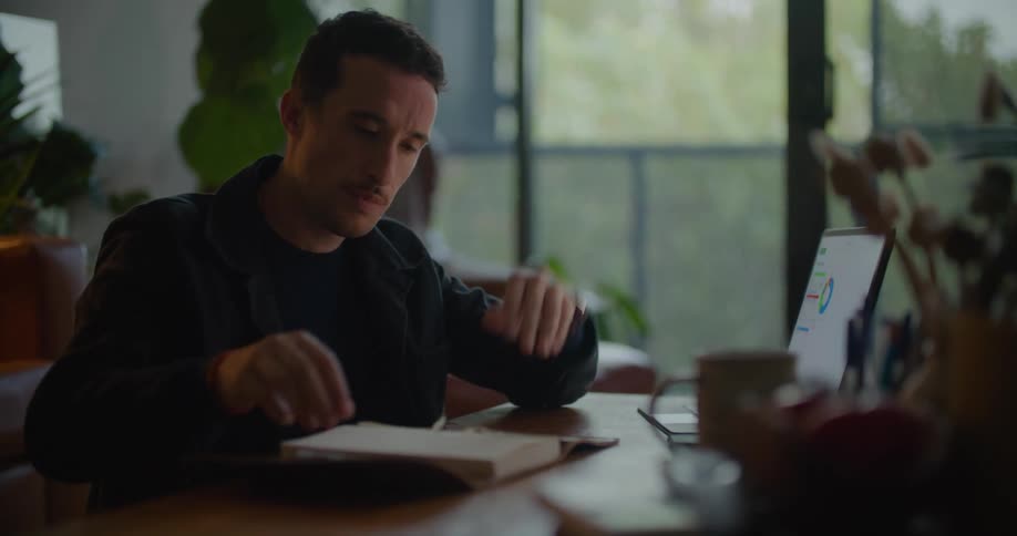 Worried man sitting at the desk using a laptop and writing on his notebook