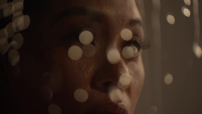 A woman stands by a window and watches the rain outside