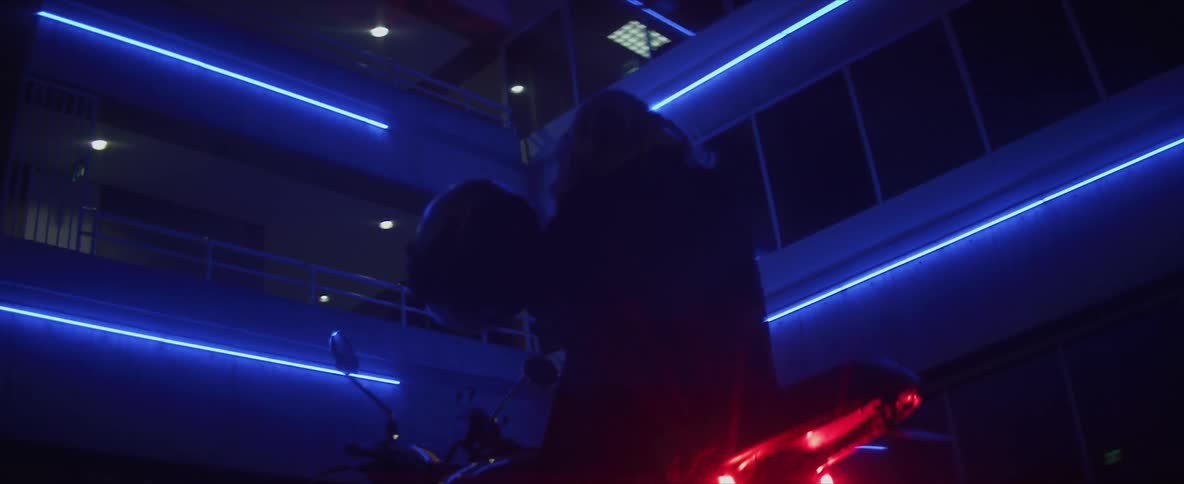 A person sitting on a motorcycle at night takes their helmet off