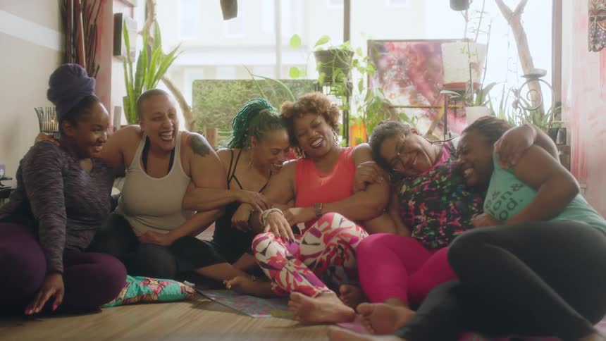 Group of women wearing sports clothes sitting on the floor hugging and laughing