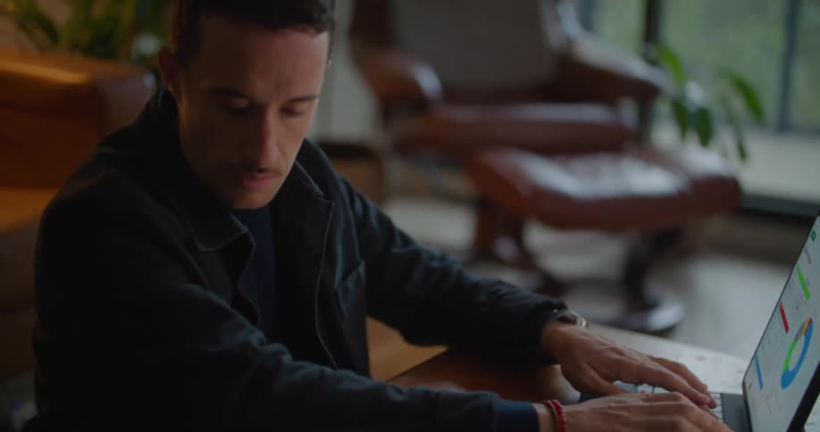 Man with naval blue jacket and shirt uses types on tablet keyboard in living room at home