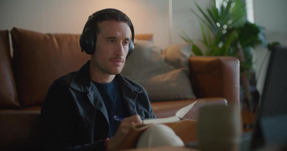 Man wears headphones while taking notes during zoom meeting