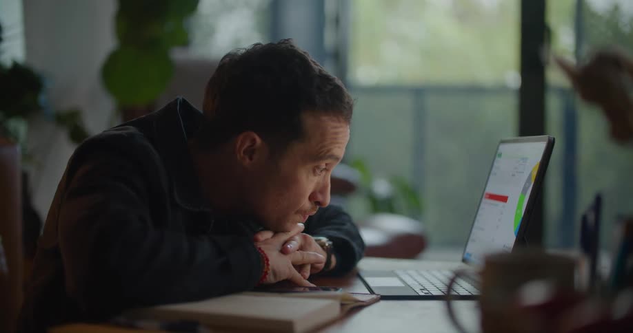 Bored man with naval blue jacket and shirt sits at desk and works on tablet