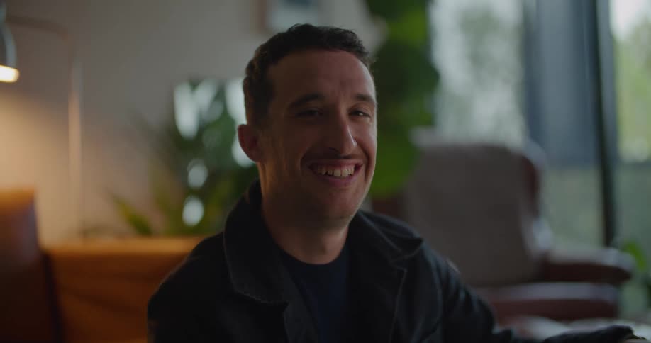 White man wearing a jacket smiling and laughing in the living room