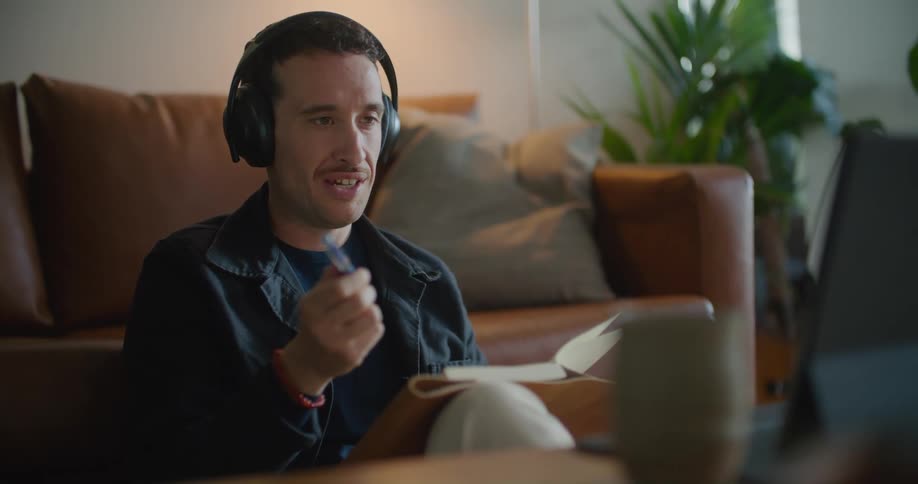 A man sitting on the floor against his couch wearing headphones and talking during a zoom business meeting