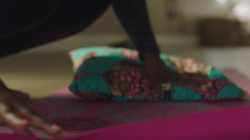 Black woman unrolling a yoga mat on the floor and then carefully putting a cushion over it