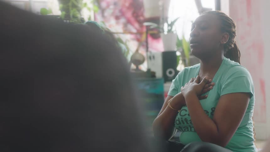 Two woman are seated with a group of others while meditating together