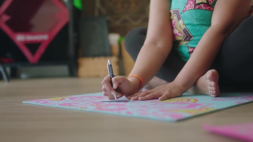 Little girl sitting on the floor writing something on a piece of paper