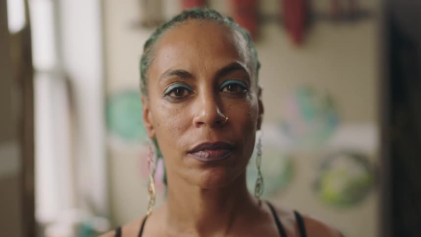 A woman standing indoors slowly opens her eyes to look into the camera